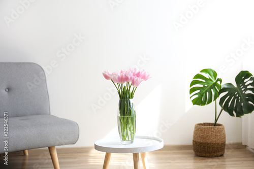 Empty apartment with minimal loft style interior  wooden floor and glass vase with bouquet of tulips on foreground and blank wall with a lot of copy space for text on background. Close up.