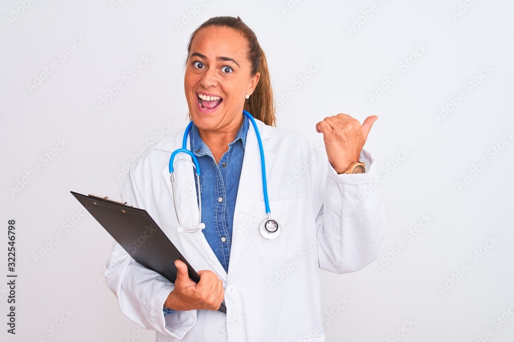 Middle age mature doctor woman holding clipboard over isolated background pointing and showing with thumb up to the side with happy face smiling Middle age mature doctor woman holding clipboard over isolated background pointing and showing with thumb up to the side with happy face smiling