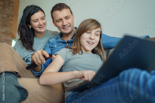 Happy family using laptop at home: mom, dad and daughter shopping online or watching funny video or movie
