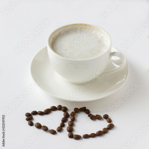 White coffee cup with plate and cofee beans in heart shape isolated on white.