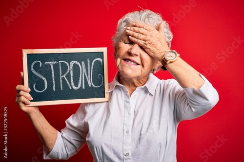 Senior beautiful woman holding blackboard with strong message over isolated red background stressed with hand on head, shocked with shame and surprise face, angry and frustrated. Fear and upset