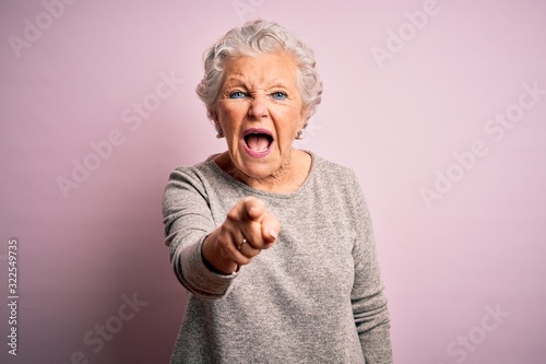 Senior beautiful woman wearing casual t-shirt standing over isolated pink background pointing displeased and frustrated to the camera, angry and furious with you photo