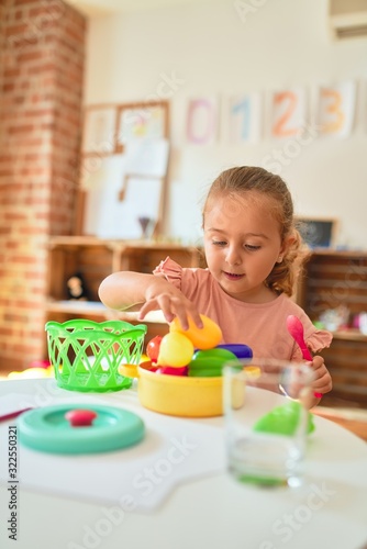 Beautiful blond toddler girl playing meals using plastic food at kindergarten