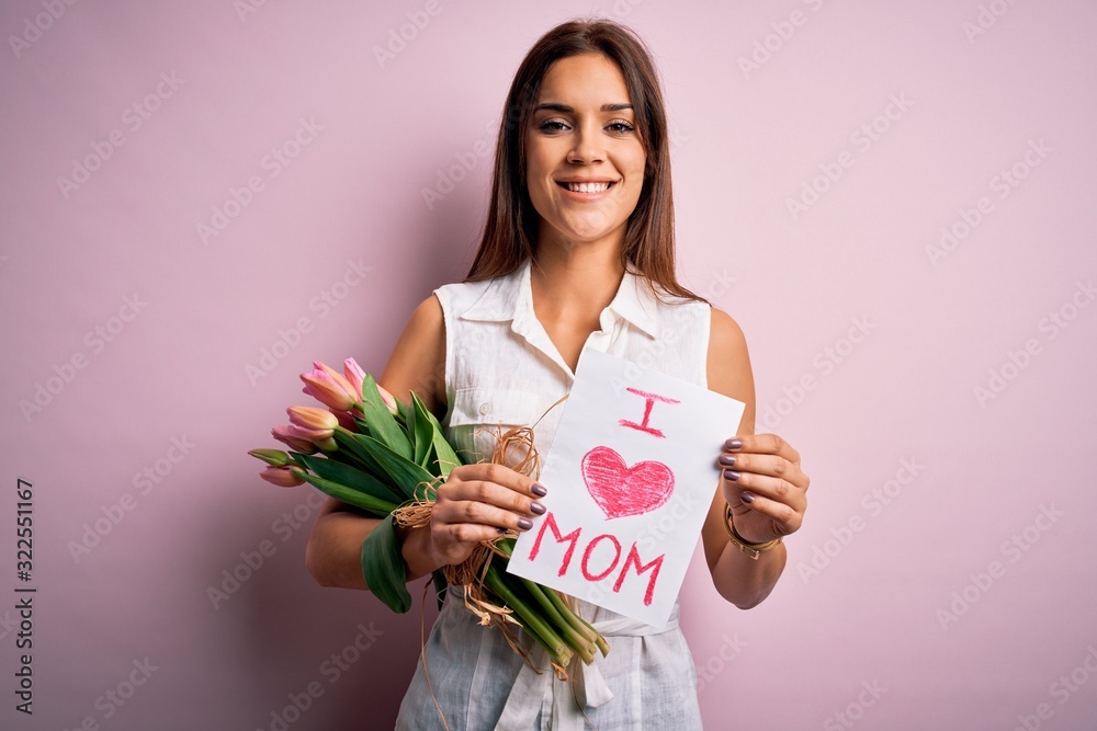 Beautiful woman celebrating mothers day holding love mom message and bouquet of tulips with a happy face standing and smiling with a confident smile showing teeth Beautiful woman celebrating mothers day holding love mom message and bouquet of tulips with a happy face standing and smiling with a confident smile showing teeth