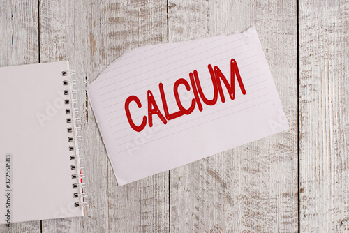 Conceptual hand writing showing Calcium. Concept meaning fifth most abundant element in the human body Silverwhite metal Torn paper and notebook sheet placed above classic wooden table photo