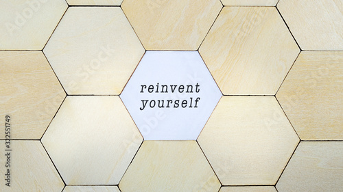 Wooden hexagon missing from puzzle, revealing the word reinvent yourself in a conceptual image of personal growth and self discovery