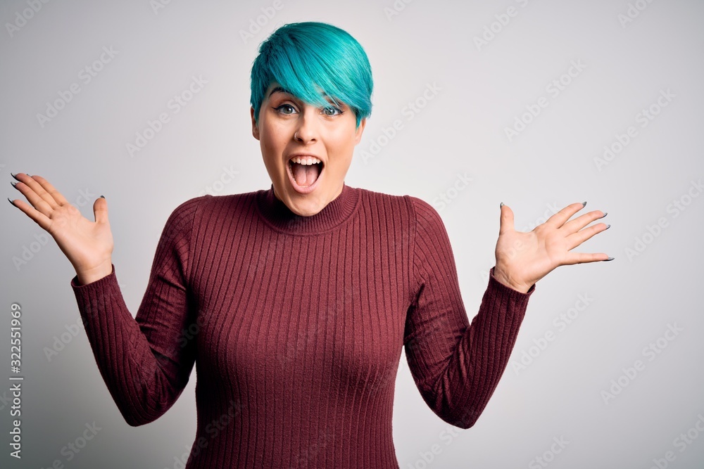 Young beautiful woman with blue fashion hair wearing casual sweater over white background celebrating crazy and amazed for success with arms raised and open eyes screaming excited. Winner concept Young beautiful woman with blue fashion hair wearing casual sweater over white background celebrating crazy and amazed for success with arms raised and open eyes screaming excited. Winner concept