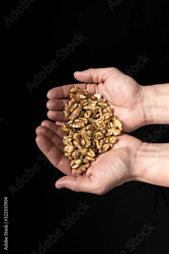 Peeled walnut kernels in male hands on a black background