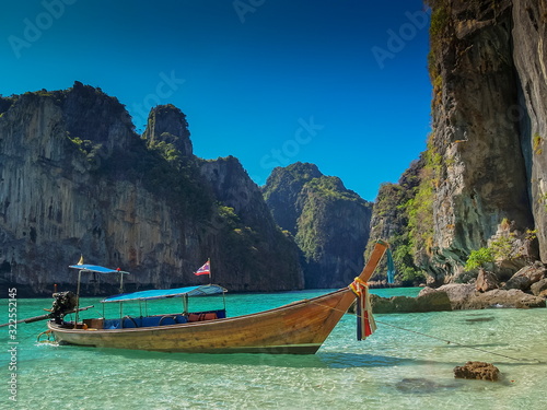 view of a long-tail boat floating in blue-green sea around with high rock mountains and blue sky background, Ao Loh Samah, Mu Ko Phi Phi islands, Krabi, southern of Thailand. © Yuttana Joe