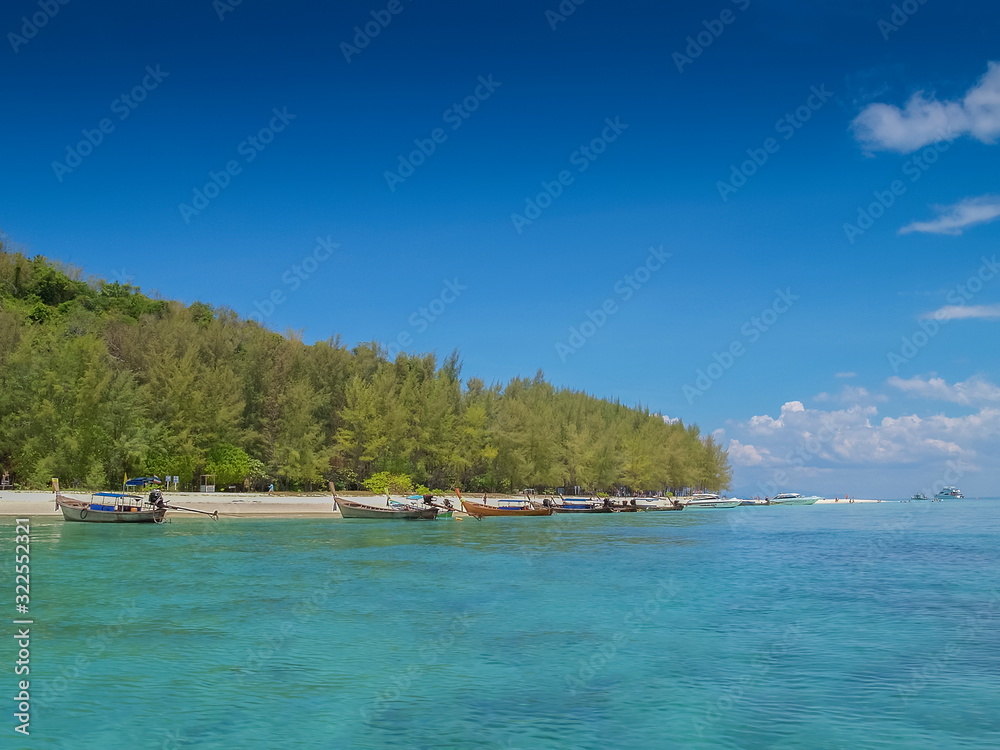 view of many long-tail boats floating seaside of green island with blue sky background, Bamboo island, Mu Ko Phi Phi islands, Krabi, southern of Thailand.