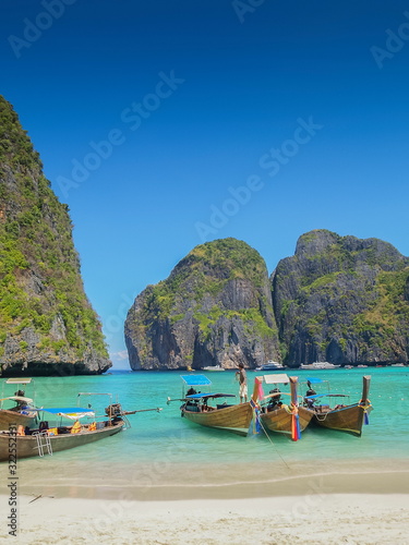 view of long-tail boats floating seaside in blue-green sea with high mountain and blue sky background, Ao Maya Bay, Mu Ko Phi Phi islands, Krabi, southern of Thailand.