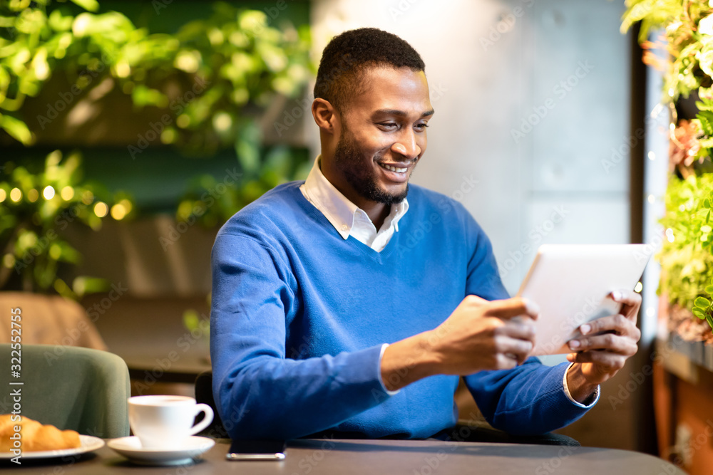 Black guy sitting in coffee shop working on his tablet Black guy sitting in coffee shop working on his tablet