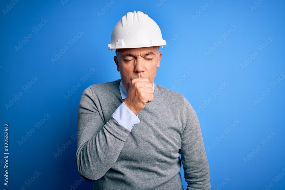 Middle age handsome grey-haired engineer man wearing safety helmet over blue background feeling unwell and coughing as symptom for cold or bronchitis. Health care concept. Middle age handsome grey-haired engineer man wearing safety helmet over blue background feeling unwell and coughing as symptom for cold or bronchitis. Health care concept.