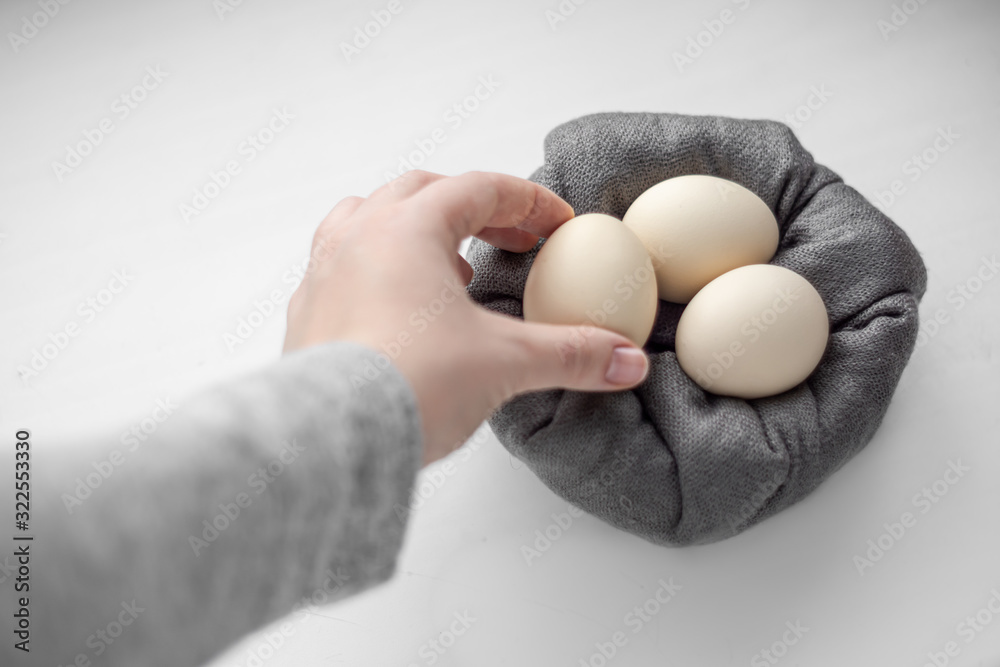 A woman's hand puts an egg in a basket with eggs.