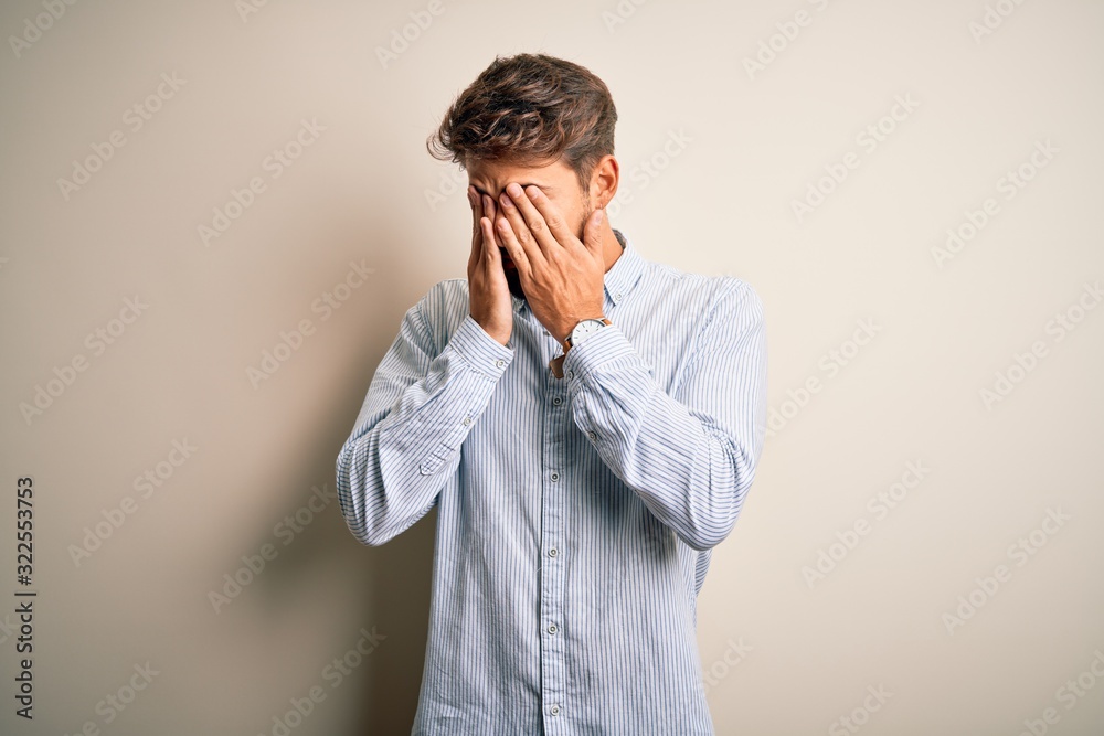 Young handsome man with beard wearing striped shirt standing over white background rubbing eyes for fatigue and headache, sleepy and tired expression. Vision problem Young handsome man with beard wearing striped shirt standing over white background rubbing eyes for fatigue and headache, sleepy and tired expression. Vision problem