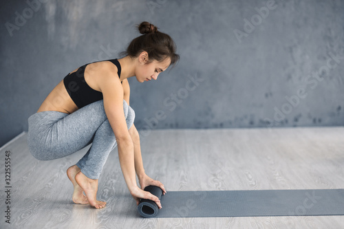 Woman rolling exercise yoga mat on wood floor