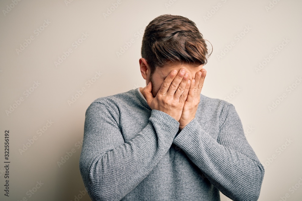 Young handsome blond man with beard and blue eyes wearing casual sweater with sad expression covering face with hands while crying. Depression concept. Young handsome blond man with beard and blue eyes wearing casual sweater with sad expression covering face with hands while crying. Depression concept.