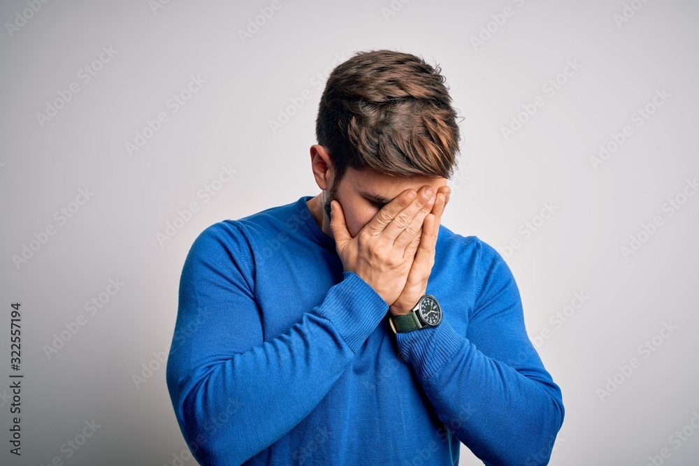 Young handsome blond man with beard and blue eyes wearing casual sweater with sad expression covering face with hands while crying. Depression concept. Young handsome blond man with beard and blue eyes wearing casual sweater with sad expression covering face with hands while crying. Depression concept.
