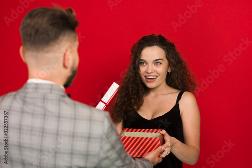 Back view of man presenting anniversary gift to pretty woman isolated on red background
