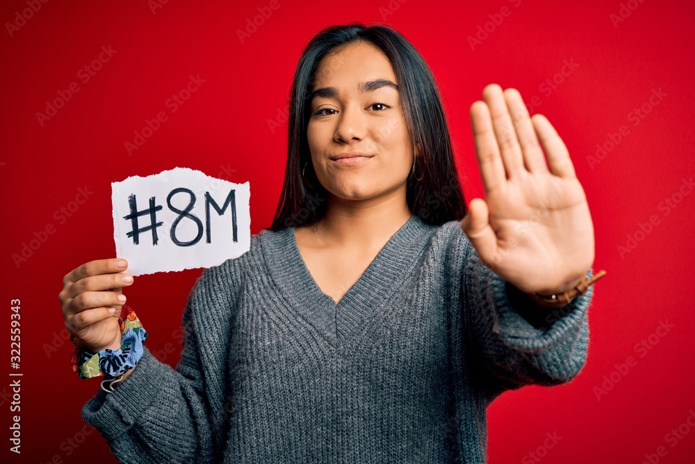 Young beautiful asian woman celebrating 8th march womens day holding reminder paper with open hand doing stop sign with serious and confident expression, defense gesture Young beautiful asian woman celebrating 8th march womens day holding reminder paper with open hand doing stop sign with serious and confident expression, defense gesture