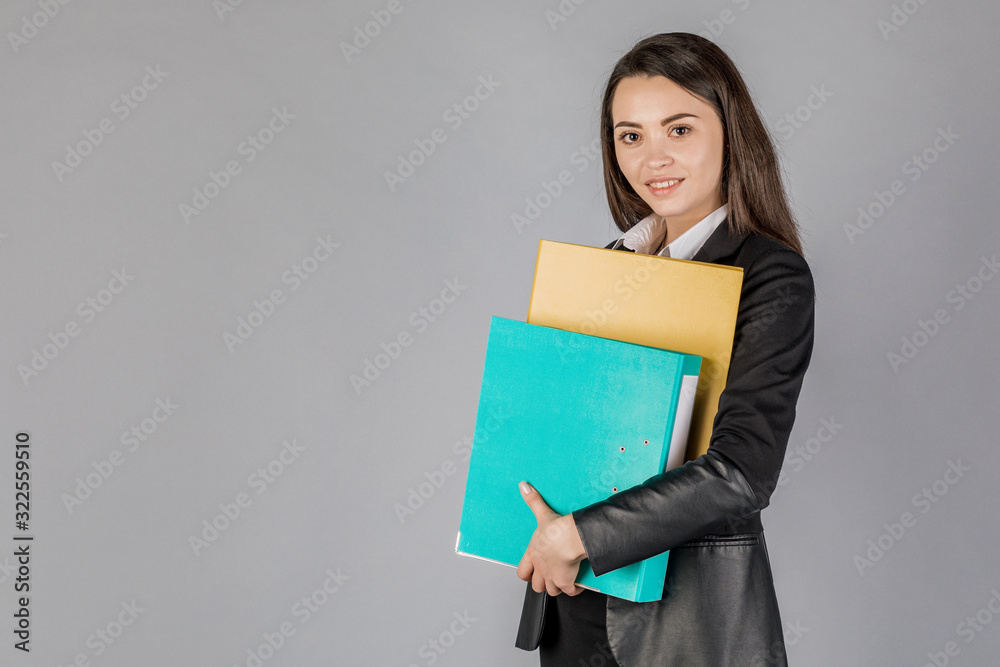 Young business woman in dark suite with files on grey background. Young business woman in dark suite with files on grey background.