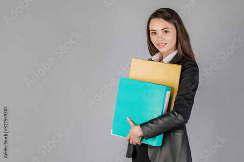Young business woman in dark suite with files on grey background.