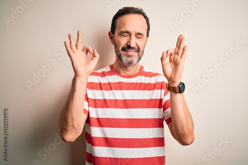 Middle age hoary man wearing casual striped t-shirt standing over isolated white background relax and smiling with eyes closed doing meditation gesture with fingers. Yoga concept.