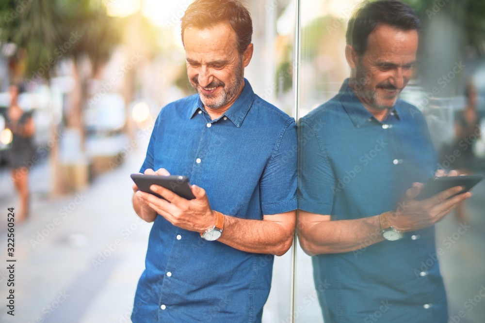 Middle age handsome businessman using tablet smiling on the street
