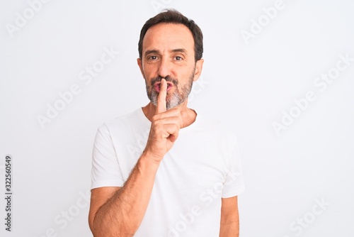 Middle age handsome man wearing casual t-shirt standing over isolated white background asking to be quiet with finger on lips. Silence and secret concept.