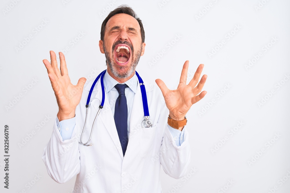 Middle age doctor man wearing coat and stethoscope standing over isolated white background celebrating mad and crazy for success with arms raised and closed eyes screaming excited. Winner concept