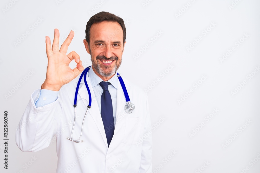 Middle age doctor man wearing coat and stethoscope standing over isolated white background smiling positive doing ok sign with hand and fingers. Successful expression. Middle age doctor man wearing coat and stethoscope standing over isolated white background smiling positive doing ok sign with hand and fingers. Successful expression.