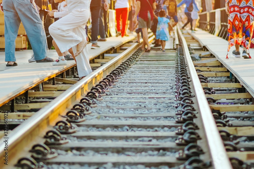 Tourists walk across across rail train tracks from side to another side while visiting The Bridge Over the River Kwai in Kanchanaburi, Thailand.