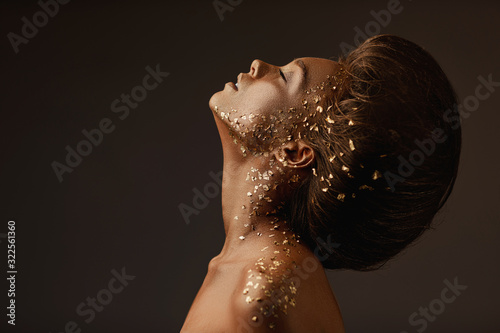 Fashion art portrait of model girl with holiday golden shiny professional makeup. beaty woman with gold metallic body and hair on dark background. Gold glowing skin. copy space photo