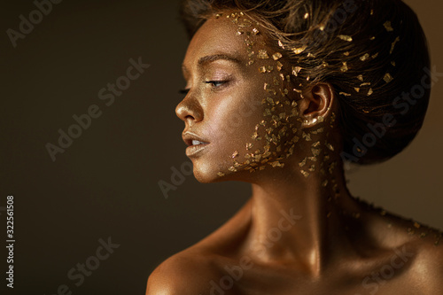 Fashion art portrait of model girl with holiday golden shiny professional makeup. beaty woman with gold metallic body and hair on dark background. Gold glowing skin. copy space photo