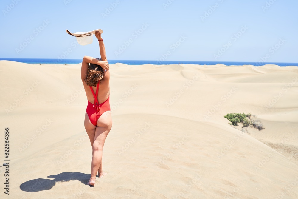 Young beautiful woman sunbathing with open arms wearing summer swinsuit at maspalomas dunes bech