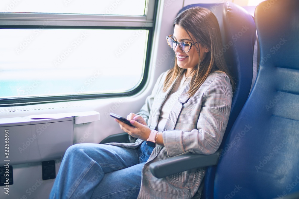 Young beautiful woman smiling happy and confident. Sitting with smile on face using smartphone travelling by train Young beautiful woman smiling happy and confident. Sitting with smile on face using smartphone travelling by train