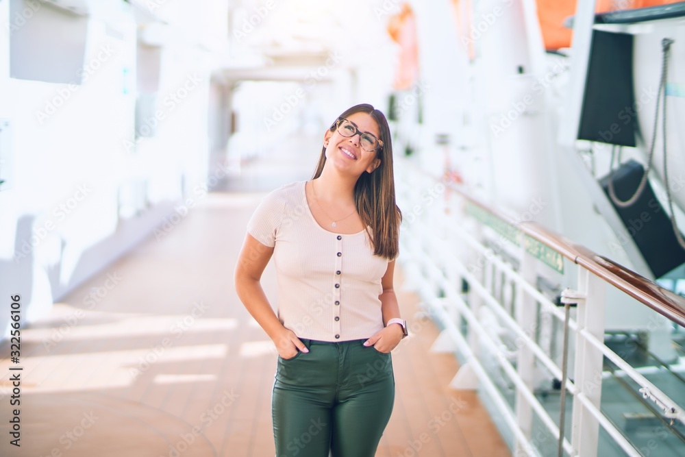 Young beautiful woman on vacation smiling happy and confident. Standing on a deck of ship with smile on face doing a cruise