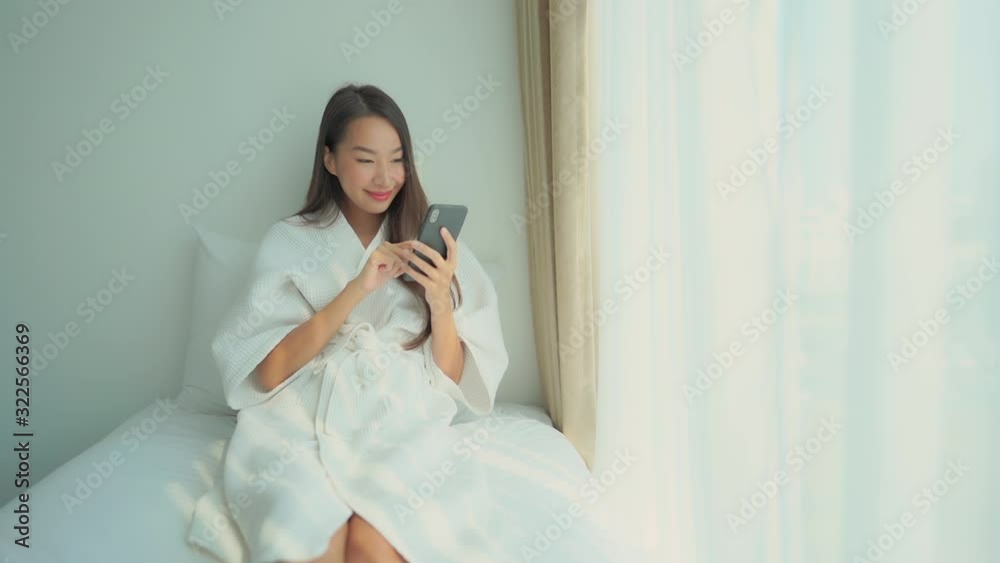 Young adult woman in bathrobe using smartphone in her bed in the morning Young adult woman in bathrobe using smartphone in her bed in the morning