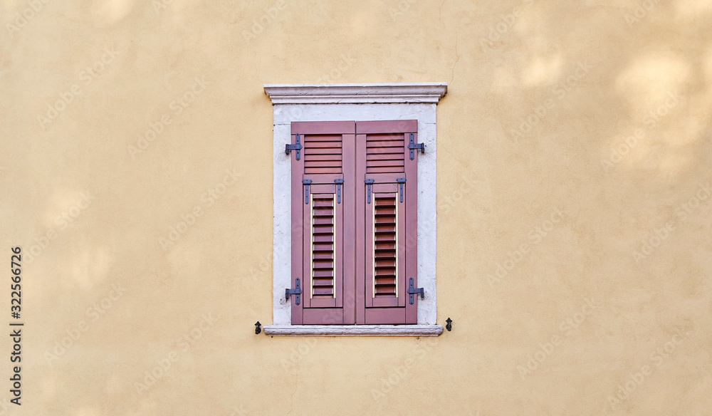 Italian windows on the yellow sandy color wall facade with closed new modern wooden red-brown color shutters