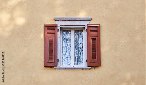 Italian windows on the yellow sandy color wall facade with open new modern wooden red-brown color shutters