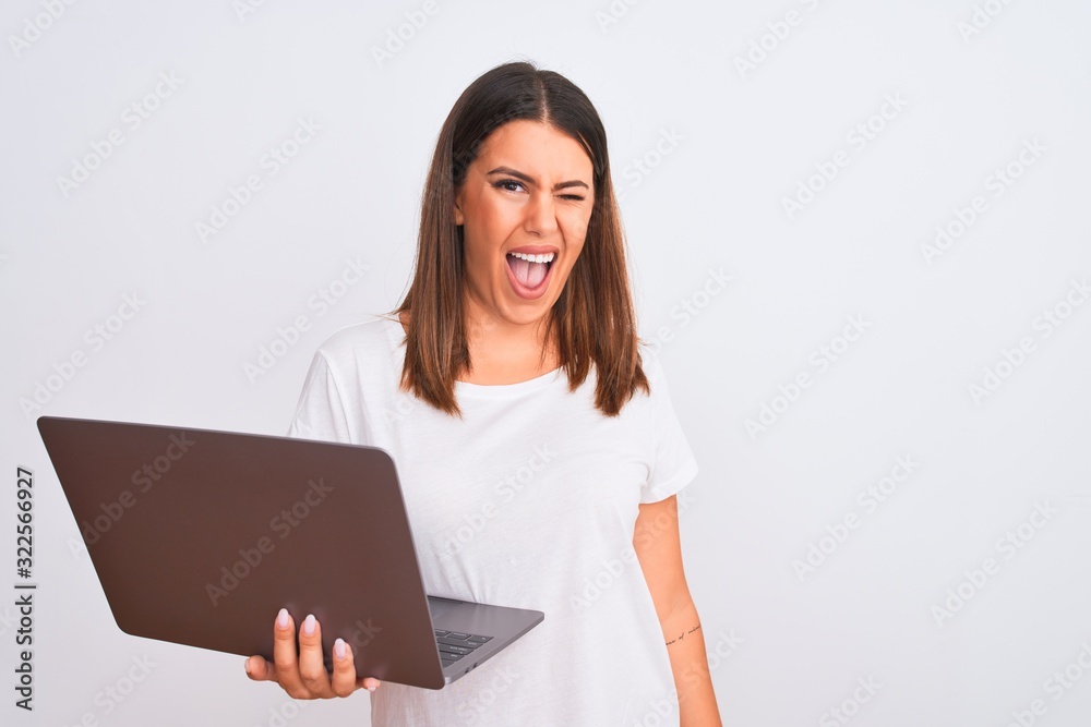 Beautiful young woman working using computer laptop over white background winking looking at the camera with sexy expression, cheerful and happy face. Beautiful young woman working using computer laptop over white background winking looking at the camera with sexy expression, cheerful and happy face.