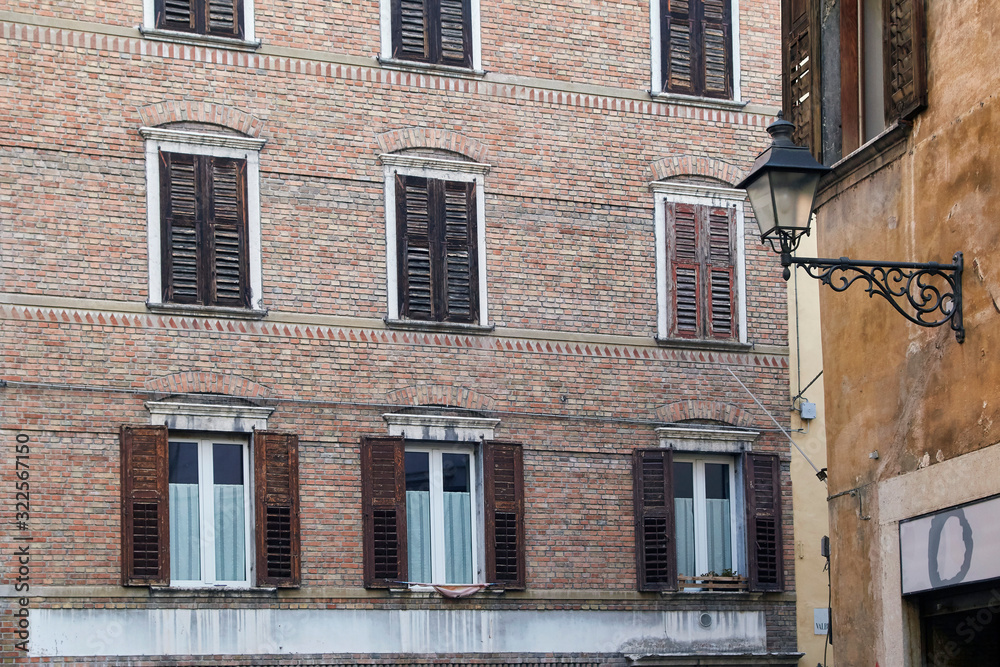 Italian windows on the vintage brick wall facade with wooden old and shabby brown color shutters