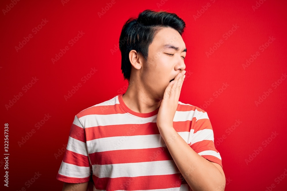 Young handsome chinese man wearing casual striped t-shirt standing over red background bored yawning tired covering mouth with hand. Restless and sleepiness. Young handsome chinese man wearing casual striped t-shirt standing over red background bored yawning tired covering mouth with hand. Restless and sleepiness.