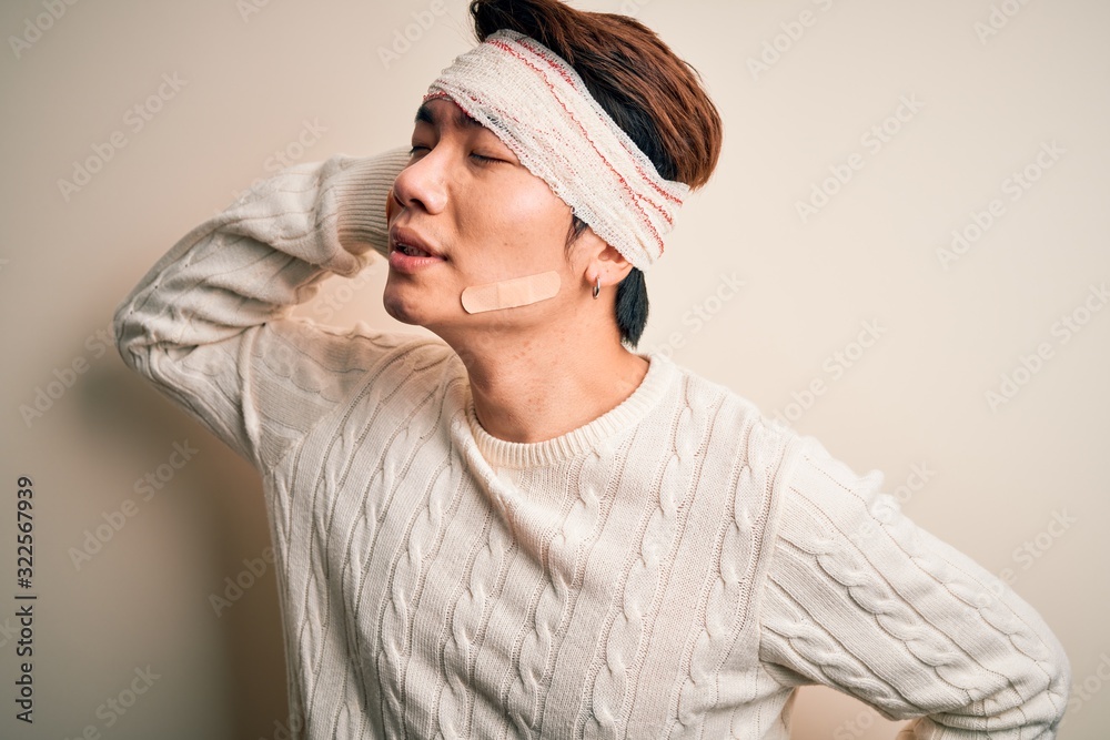 Young handsome chinese man injured for accident wearing bandage and strips on head Suffering of neck ache injury, touching neck with hand, muscular pain Young handsome chinese man injured for accident wearing bandage and strips on head Suffering of neck ache injury, touching neck with hand, muscular pain