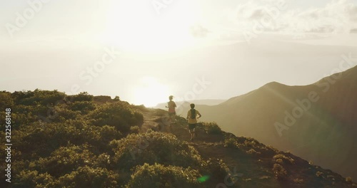 Aerial view of two runners exploring a mountain ridge top at sunset, young adventurous couple running on an amazing trail in the mountains photo