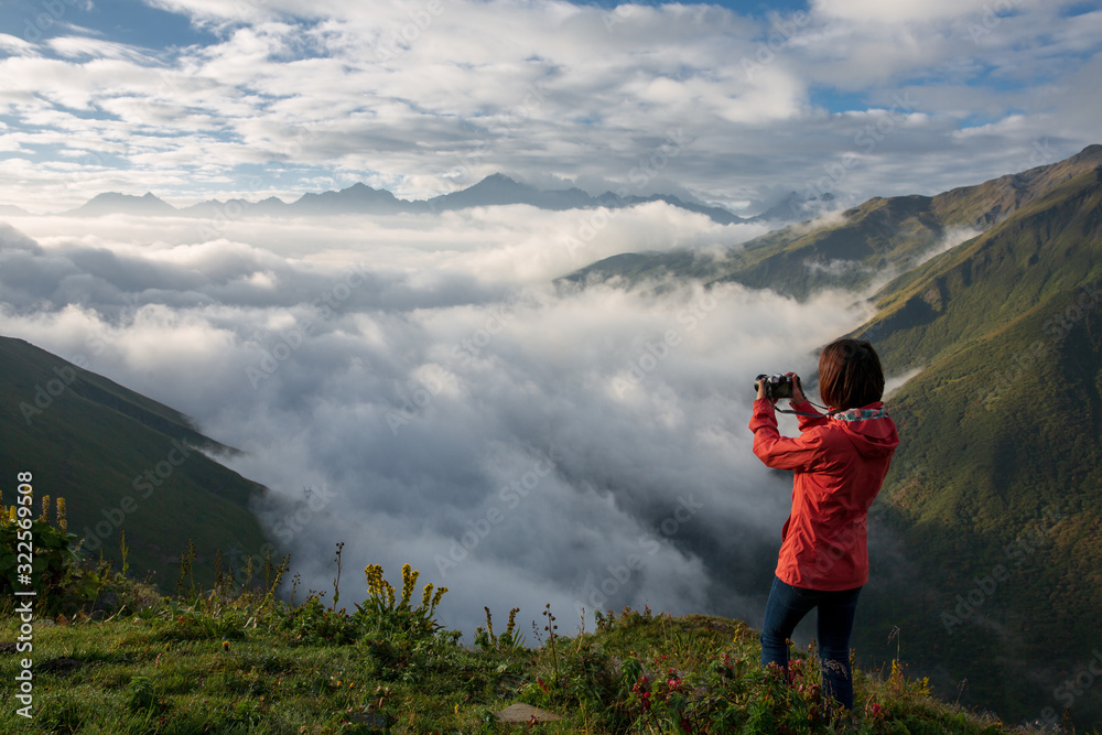 An unidentified woman wearing red jacket standing on a mountain peak above the clouds