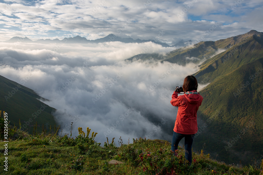 An unidentified woman wearing red jacket standing on a mountain peak above the clouds