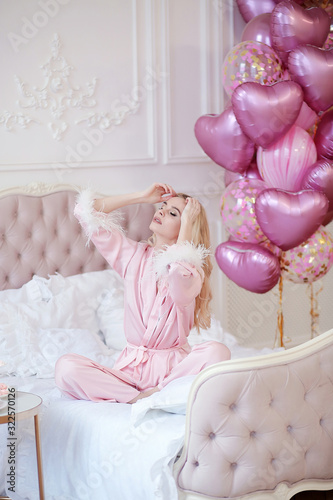 Beautiful blonde girl has breakfast in bed. Girl in pink pajamas in a light interior. Tender bride morning