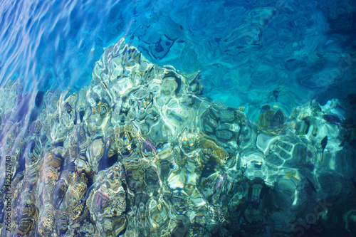 Coral reef in a bright blue sea from above with sun glare on the surface of the water