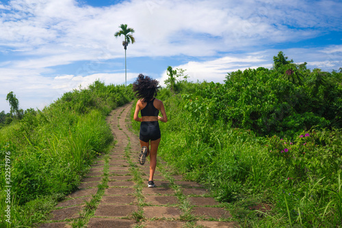 rear view female runner training on countryside road - young attractive and fit jogger woman doing running workout outdoors at beautiful track in healthy lifestyle